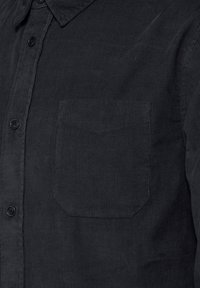 Svart kordfluroskjorta med knappstängning framtill, spetsig krage och en enda bröstficka med en subtil struktur av tyget.