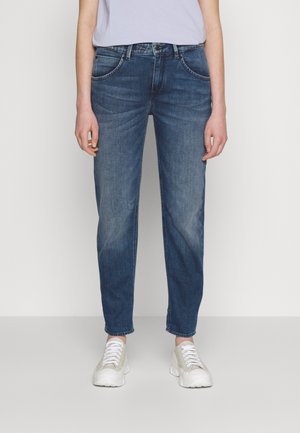Blue denim jeans with a relaxed fit, straight legs, and front pockets. Paired with light grey sneakers and a simple top.