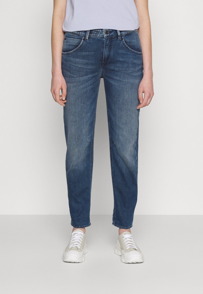 Jeans de denim azul con un corte relajado, piernas rectas y bolsillos delanteros. Combinados con zapatillas ligeras de color gris y una blusa sencilla.
