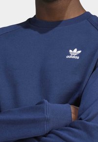 Sudadera azul marino hecha de una mezcla de algodón con cuello redondo acanalado, mangas con puños y logo blanco de Adidas en el pecho.