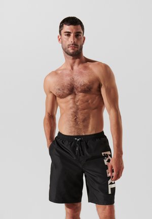 Schwarze Schwimmshorts mit elastischem Bund und Kordelzug, die entlang der Seite ein großes Logo in einer kontrastierenden Farbe aufweisen.