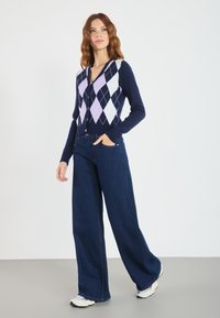 Mørkeblå cardigan med argyle-mønster i lavendel og hvit, kombinert med vide mørk denimjeans og hvite sneakers.