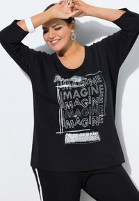 Maglietta nera con scollatura rotonda e maniche a tre quarti, caratterizzata da una grafica ripetuta "IMAGINE" in bianco con accenti testurizzati.