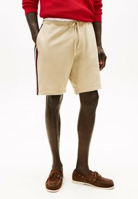 Shorts di cotone beige con vita regolabile, caratterizzati da strisce laterali in navy e rosso. Indossati con scarpe mocassino marroni.