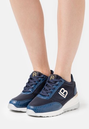 Baskets bleu marine avec panneaux texturés et logo "LB" portées pieds nus sur fond blanc.