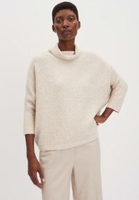 Maglione beige a collo alto con vestibilità rilassata, realizzato in un morbido tessuto strutturato. Le maniche sono a tre quarti con polsini a costine.