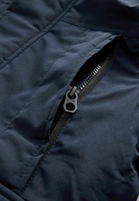 Tissu de veste isolée bleu marine avec un gros plan d'une fermeture éclair noire, mettant en avant la texture lisse et les coutures détaillées le long de la couture.