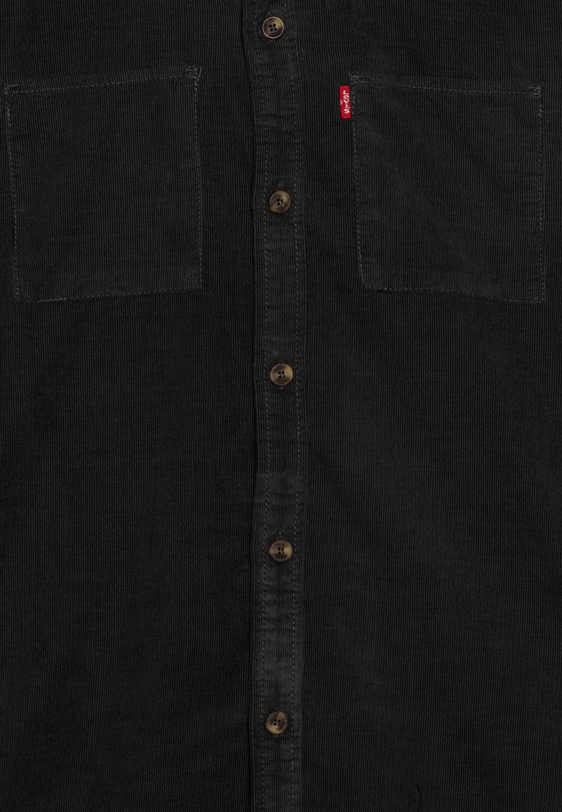 Camicetta in corduroy nera con due tasche sul petto e cinque bottoni marroni sul davanti, con un piccolo etichetta rossa Levi's sulla tasca destra.