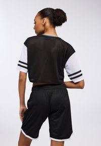 Top corto a maniche corte in rete nera con dettagli e righe bianche, abbinato a pantaloni corti in rete nera con bordo bianco all'orlo.