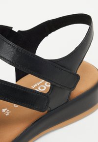 Black leather sandal with adjustable straps, textured finish, cushioned footbed, and a light brown sole featuring brand logo in white.