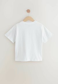 Weißes Baumwoll-T-Shirt mit kurzen Ärmeln, Rundhalsausschnitt und geradem Schnitt, das an einem Holzkleiderbügel vor einem hellen Hintergrund hängt.