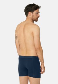 Mörkblå bomullsboxershorts med en mjuk midja, med en slät yta och kroppsnära design. Synlig tatuering på armen.