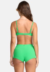 Groene geribde bikinitop met verstelbare bandjes en bijpassende hoge shorts. De soepele textuur en het aansluitende ontwerp accentueren de silhouet.