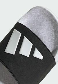 Black slide sandal with three white geometric accents on the strap, textured upper, and a smooth, white rubber sole.