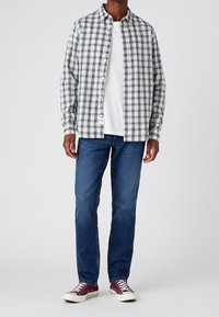 Overhemd met knopen in blauw-witte ruit, gedragen over een wit T-shirt. Gecombineerd met blauwe spijkerbroek en bordeauxrode sneakers. Gladde stof, lange mouwen.