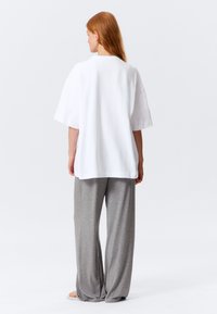 White oversized T-shirt with a round neckline, paired with gray wide-leg pants, both made of soft fabric, viewed from the back.
