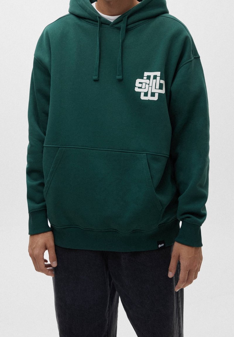 Sudadera de color verde oscuro hecha de una tela suave, con un bolsillo frontal, capucha ajustable y un detalle de logo blanco en el lado izquierdo del pecho.