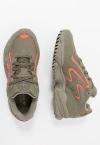 Buty sportowe w oliwkowym kolorze z koralowymi akcentami. Siatkowa i zamszowa cholewka, okrągły nosek, sznurowana konstrukcja, gumowa podeszwa z wzorami zapewniającymi przyczepność.