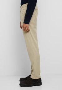 Beige katoenen broek met een rechte pasvorm, omgeslagen zoom, zijzakken en een achterzak, gecombineerd met donker leren enkellaarsjes.