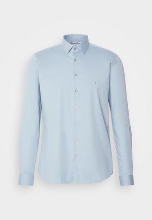 Cămașă albastră deschis, cu mânecă lungă și nasturi, confecționată dintr-un material fin, cu guler clasic și un logo mic brodat pe piept.