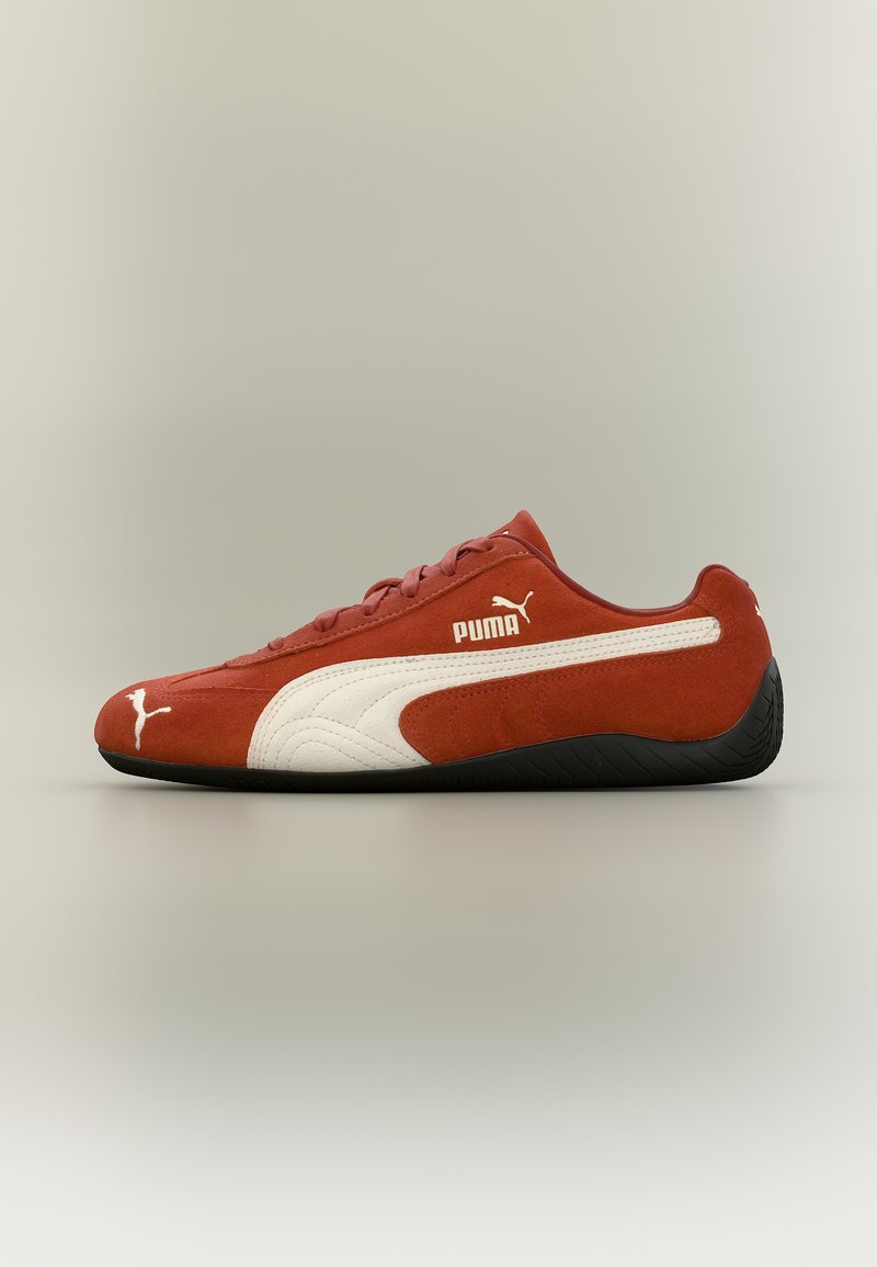 Κόκκινο αθλητικό παπούτσι Puma με διακριτικό προφίλ, λευκή λωρίδα στο πλάι, λογότυπο Puma στο πλάι και στο δάχτυλο, και μαύρη σόλα σε ουδέτερο φόντο.