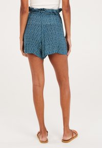 Pantaloni corti blu a fantasia con vita arricciata, orlo asimmetrico e tessuto leggero, abbinati a sandali marroni.