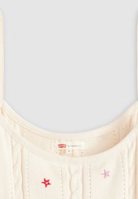 Cremefarvet striktrøje med kabelmønster, justerbare stropper og broderede stjerner i rød og pink. Mærket siger "Levi's," størrelse S.