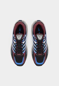 Ζευγάρι πολύχρωμα αθλητικά παπούτσια με μαύρο διχτυωτό υλικό, μπλε και μαρουαν αποχρώσεις, και μαύρα κορδόνια, εμφανιζόμενα από πάνω σε λευκό φόντο.