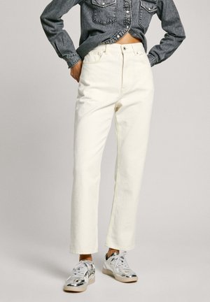 Jeans blancos de cintura alta con un diseño de pierna recta y costura amarilla, combinados con zapatillas plateadas. La parte superior es una camisa de mezclilla oscura.