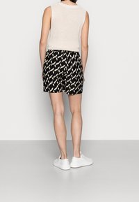 Shorts noirs avec un motif zigzag crème, dotés d'une taille élastique. Associés à un haut en tricot léger sans manches et des baskets blanches.
