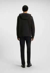 Svart hoodiejacka med dragsko i huvan, slät tyg och en avslappnad passform. I kombination med svarta byxor och platta svarta skor.