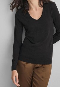 Pull noir à manches longues avec un col en V, fabriqué dans un matériau doux. Présente une silhouette ajustée et un ourlet côtelé. Associé à un pantalon marron de style satin.