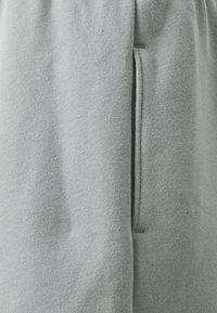 Pantaloni di tessuto grigio con una texture liscia, dotati di una tasca laterale e una vestibilità comoda, che mostrano un design pulito senza embellimenti.