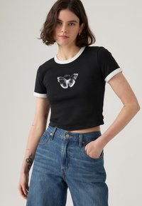 Μαύρο κοντό t-shirt με λευκές λεπτομέρειες στο γιακά, στο κέντρο φέρει σχέδιο πεταλούδας. Συνδυασμένο με ψηλόμεσο μπλε τζην παντελόνι.