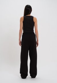 Top smanicato nero a costine abbinato a pantaloni di tuta neri larghi. Il tessuto sembra morbido con una vita elastica e una vestibilità comoda.