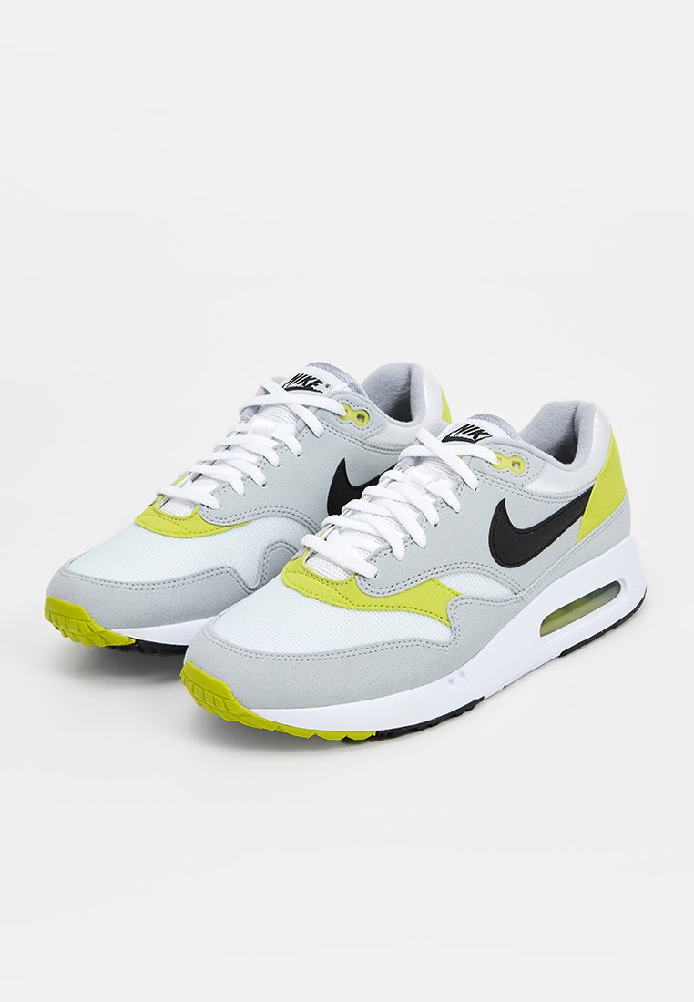 Nike sneakers in grijs en geel, met een mix van mesh en suède materialen, een zwart Swoosh-logo en een zichtbare luchtunit in de zool.