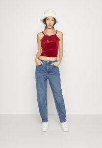 Top cropped de veludo vermelho com um detalhe bordado a dourado, combinado com jeans de cintura alta em azul claro e ténis brancos, além de um chapéu de balde branco.