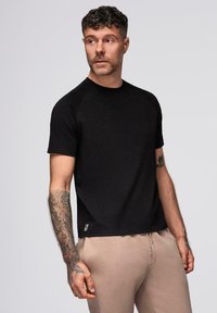 Sort kortærmet t-shirt med rund hals, der har raglan ærmer og en subtil tekstur. Lille logoetiket nær sømmen.