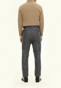 Beige tröja med hög krage, ihop med skräddarsydda grå ullbyxor med sidofickor och en avslappnad passform. Svarta läderskor bärs.