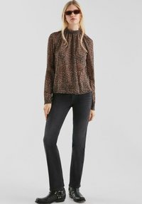 Bluzka z długim rękawem i wysokim kołnierzem w ciemny kwiatowy wzór, zestawiona z czarnymi jeansami slim fit oraz czarnymi botkami za kostkę z klamerkami. Okulary przeciwsłoneczne dopełniają całość.
