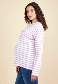 Stribet graviditetstop i hvid og lyserød, med lange ærmer og en afslappet pasform, parret med blå denim jeans.
