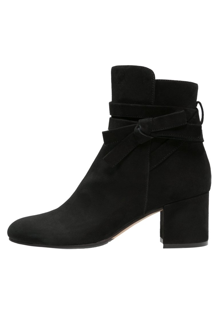 Bottine en daim noir avec talon carré, sanglon enveloppant noué en nœud, et bout arrondi, vue de côté extérieur.