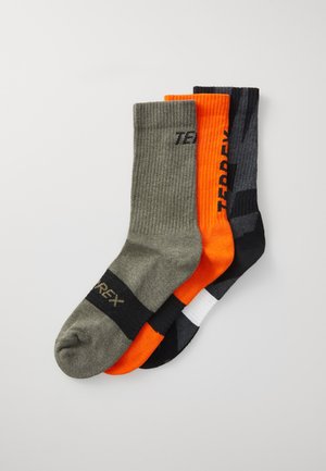 Drie paar sokken: olijfgroen, levendig oranje en zwart. Elk heeft een geribbelde textuur en duidelijke merklettering.