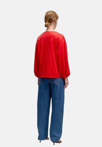 Roter übergroßer Pullover mit Ballonärmeln, kombiniert mit hoch taillierten blauen weiten Jeans. Der Stoff wirkt weich mit einer glatten Textur.