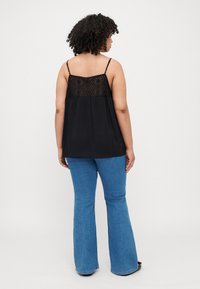 Haut sans manches noir avec un dos en dentelle et un design fluide, associé à un jean flare bleu clair. Tissu lisse avec des détailsintriqués.