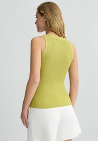 Top a costine senza maniche di colore verde chiaro, con tagli sulle spalle e una piccola etichetta logo sulla parte posteriore. Indossato con pantaloni corti bianchi.