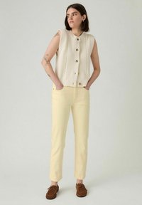 Chaleco de punto crema con textura acanalada y botones de madera, combinado con pantalones ajustados amarillos pálidos y zapatos mocasín marrones.