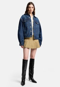 Kurtka dżinsowa o luźnym kroju, z dużymi przednimi kieszeniami i zapięciem na guziki. Nosi się ją na kremową bluzkę i plisowaną khaki spódnicę, w zestawie z czarnymi kozakami sięgającymi kolan.