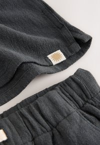Prenda de tela texturizada de color gris oscuro con cintura elástica y pequeña etiqueta blanca con un símbolo de sol beige en el borde de la prenda.