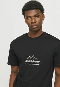 Sort bomulds T-shirt med et trekantet grafisk design og tekstlogo i hvid, med rund halsudskæring og korte ærmer.
